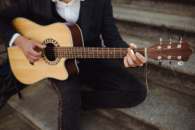 Zbliżenie na męskie dłonie gry na gitarze akustycznej na schodach