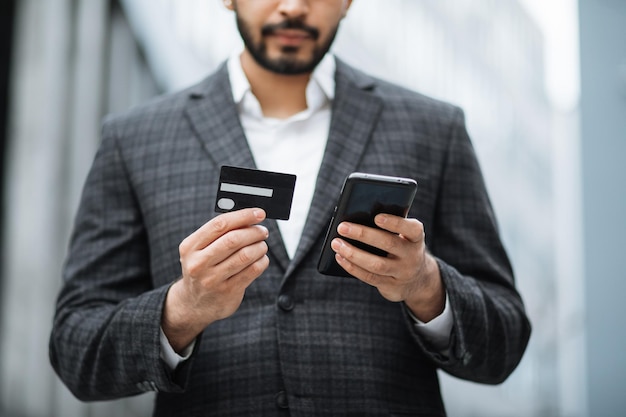 Zbliżenie na męskie dłonie trzymające smartfon i kartę kredytową