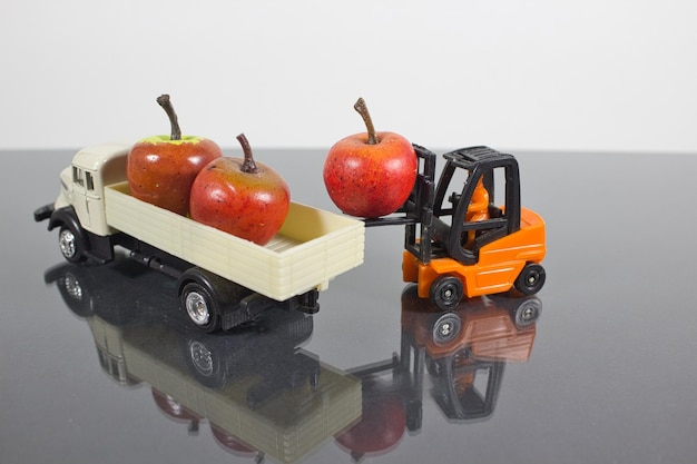 Zbliżenie na miniaturową postać pracownika wózka widłowego rozładowującego jabłka w ciężarówce