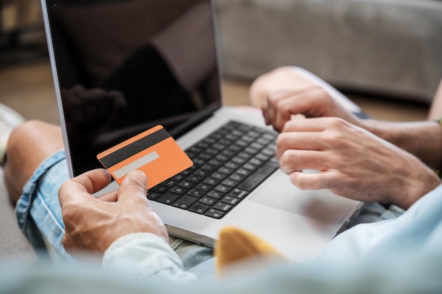 Zbliżenie Na Nierozpoznawalną Parę Gejów Za Pomocą Laptopa Siedząc Na Kanapie W Domu, Robiąc Zakupy Online Za Pomocą Karty Kredytowej