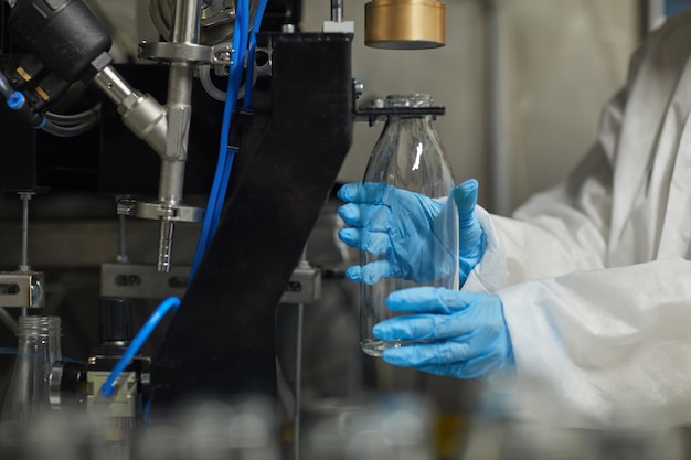 Zbliżenie na nierozpoznawalną pracownicę dezynfekującą butelki podczas pracy w fabryce żywności, miejsce kopiowania