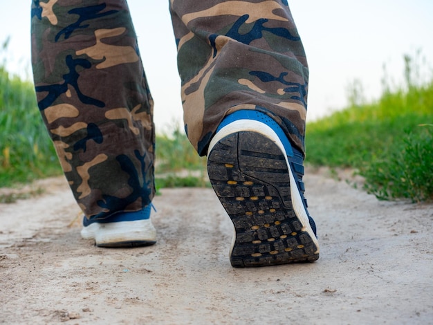 Zbliżenie na nogi mężczyzny ubranego w tenisówki idącego ścieżką w lesie. Pojęcie wędrówek, spacerów i sportowego stylu życia. widok z tyłu