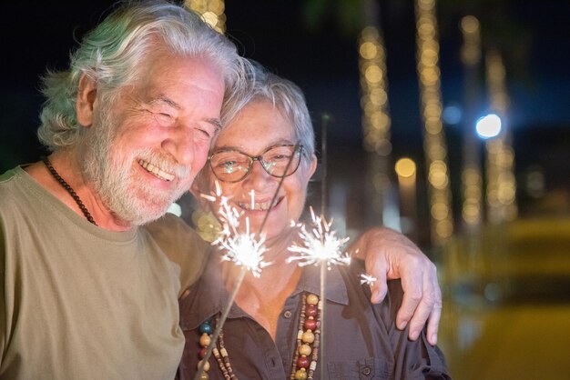 Zbliżenie na piękną parę starszych w plenerze w nocy, bawiąc się błyszczy światłami Dwóch uśmiechniętych emerytów przytulających się z miłością