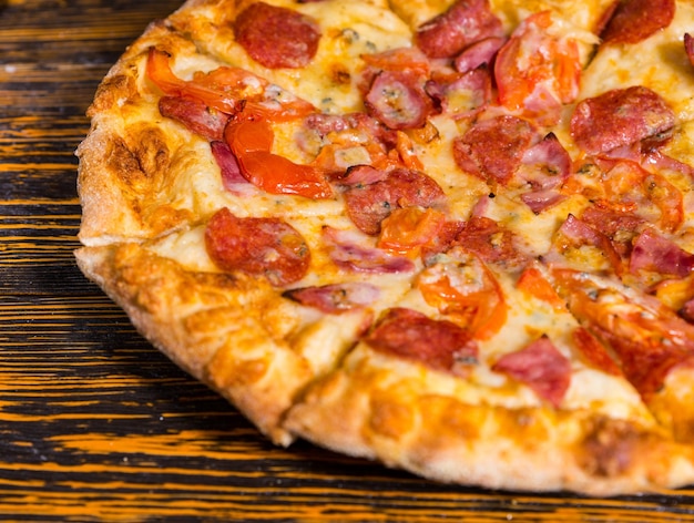 Zbliżenie na pizzę z szynką, pepperoni, pomidorami i sosem na drewnianym stole