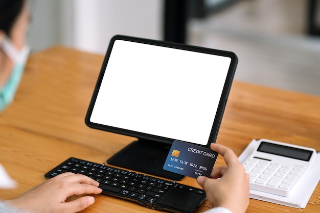 Zbliżenie na ręce kobiety trzymając kartę kredytową i za pomocą laptopa, tabletu pusty biały ekran. Koncepcja zakupów online.