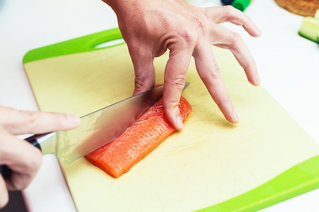 Zbliżenie na ręce osoby nie do poznania cięcia surowego i świeżego łososia nożem w deskę do krojenia