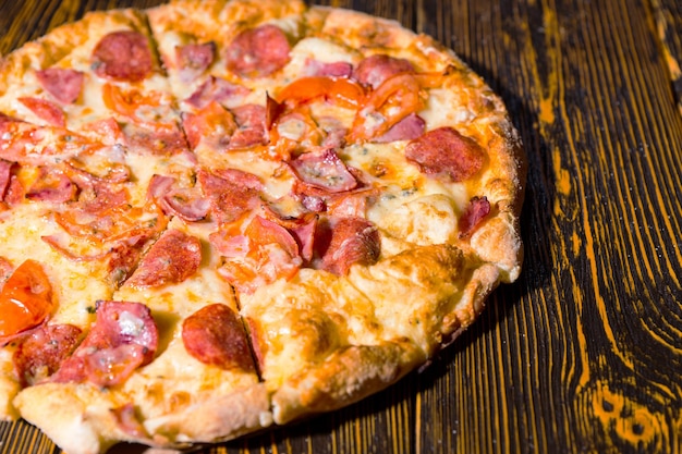 Zbliżenie na smaczną pizzę z szynką, pepperoni, pomidorami i sosem na drewnianym stole