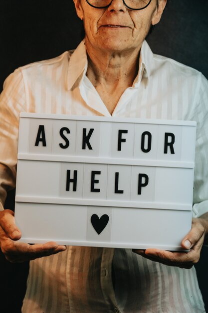 Zbliżenie na starą kobietę trzymającą znak z napisem „Poproś o pomoc”, uśmiechając się do kamery, koncepcji wsparcia zdrowia psychicznego i depresji