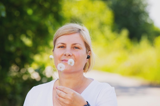 Zdjęcie zbliżenie na szczęśliwą wysportowaną blond kobietę na zewnątrz, noszącą inteligentny zegarek i słuchawki, trzymającą...