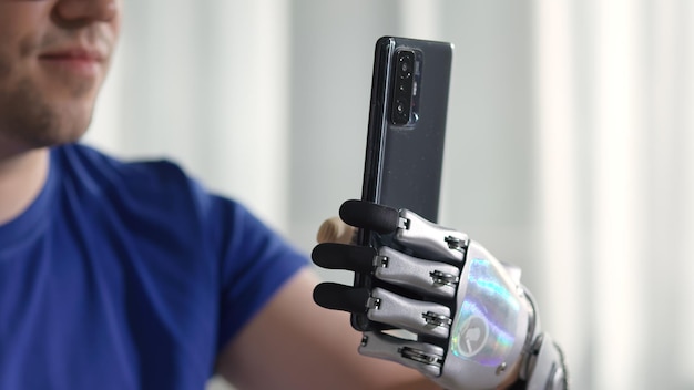 Zbliżenie na szczęśliwego młodego człowieka z nowoczesnym ramieniem bionicznym za pomocą telefonu komórkowego do czytania wiadomości