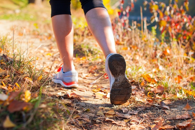 Zbliżenie na szczupłe kobiece nogi biegające po ziemi z suchymi liśćmi, noszące sportowe buty
