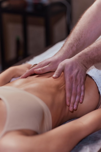 Zbliżenie na terapeutę wykonującego masaż brzucha na kobiecie w spa na ciemnym tle