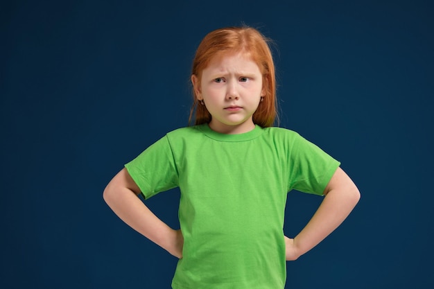 Zbliżenie na zdjęcie małej rudowłosej emocjonalnej dziewczyny pozującej przed kamerą na niebieskim tle