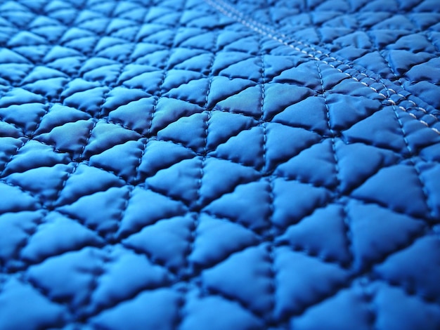 Zbliżenie niebieskiej syntetycznej pikowanej tkaniny przeciwdeszczowej Szwy maszynowe są szyte w kilku kierunkach, aby uzyskać efekt objętości i struktury Przemysł tekstylny Abstrakcyjne tło z gradientem