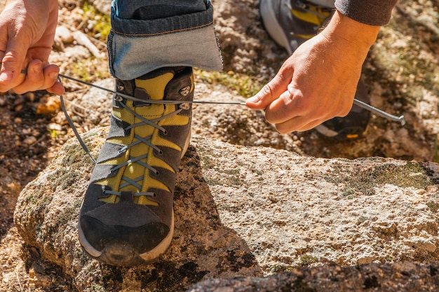 Zbliżenie nierozpoznawalnego mężczyzny wiążącego sznurówki butów trekkingowych na granitowej skale