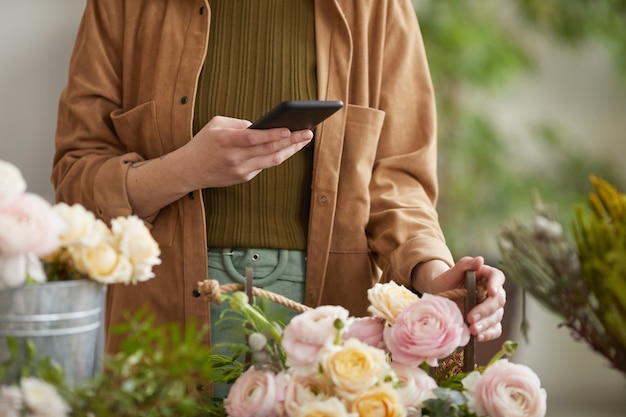 Zbliżenie nierozpoznawalnej kobiecej kwiaciarni robiącej zdjęcia kompozycji kwiatowych za pomocą smartfona podczas pracy w kwiaciarni, kopia przestrzeń