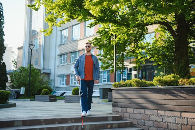 Zbliżenie niewidomego mężczyzny stojącego z białym kijem na ulicy