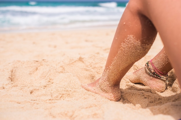 Zbliżenie nogi kobiety zrelaksowany na plaży, ciesząc się przyrodą i piaskiem z falami i oceanem - nudyzm i koncepcja wakacji dla kobiet rasy kaukaskiej