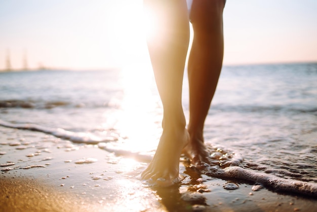 Zbliżenie nogi młodej kobiety idącej wzdłuż fali wody morskiej i piasku na letniej plaży