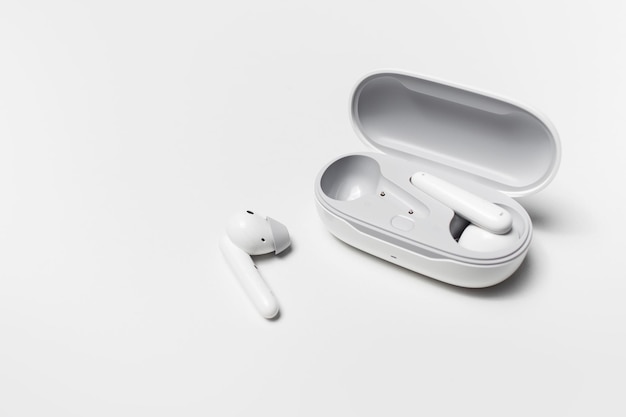 Zbliżenie nowoczesnych bezprzewodowych słuchawek i otwartej skrzynki ładującej na białym tle