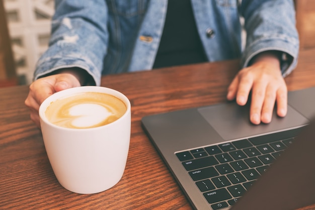 Zdjęcie zbliżenie obraz kobiety za pomocą i dotykając laptopa touchpad na drewnianym stole podczas picia kawy