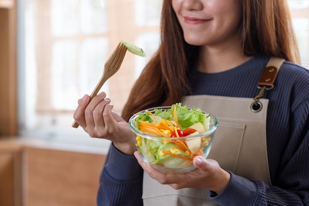 Zbliżenie obraz młodej kobiety gotowanie i jedzenie sałatki ze świeżych warzyw mieszanych w domu