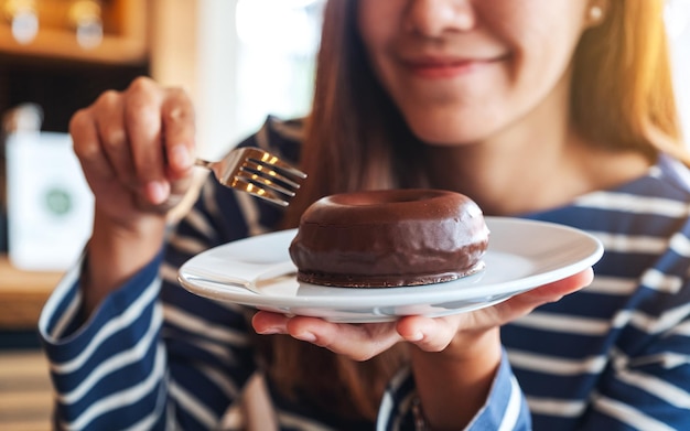 Zbliżenie obraz pięknej młodej azjatyckiej kobiety trzymającej i jedzącej czekoladowego pączka