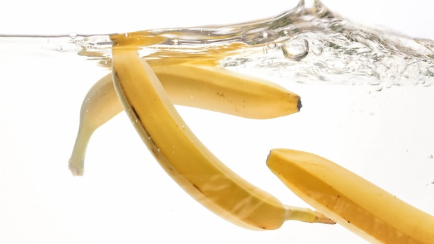 Zdjęcie zbliżenie obraz świeżych dojrzałych bananów spadających i rozpryskujących się w wodzie na białym odosobnionym tle