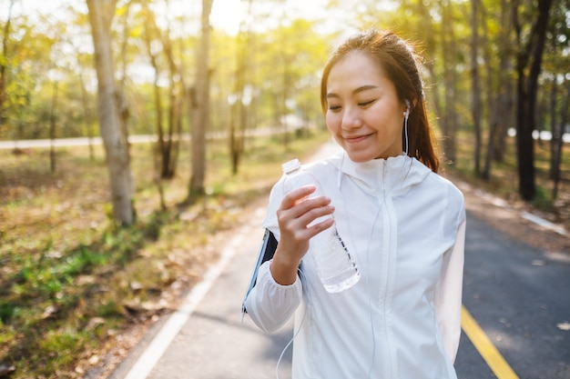 Zbliżenie obrazu azjatyckiej biegaczki trzymającej i pijącej wodę z butelki po joggingu w parku miejskim