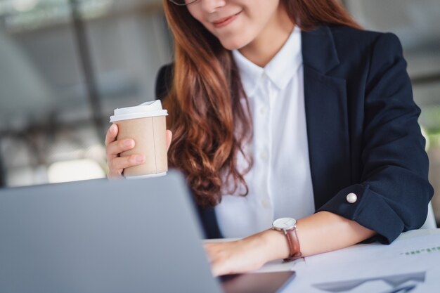 Zbliżenie obrazu bizneswoman trzymającej filiżankę kawy podczas pracy na laptopie w biurze