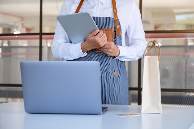 Zbliżenie obrazu kobiecej kasjerki za pomocą cyfrowego tabletu i laptopa z torbą na zakupy i kartą kredytową na biurku kasjera