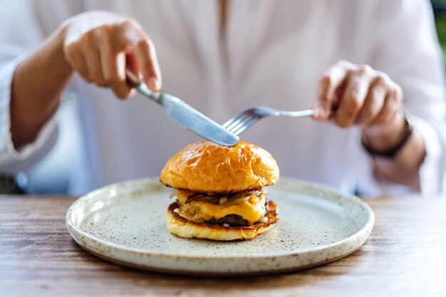 Zbliżenie obrazu kobiety jedzącej hamburgera wołowego z nożem i widelcem w restauracji