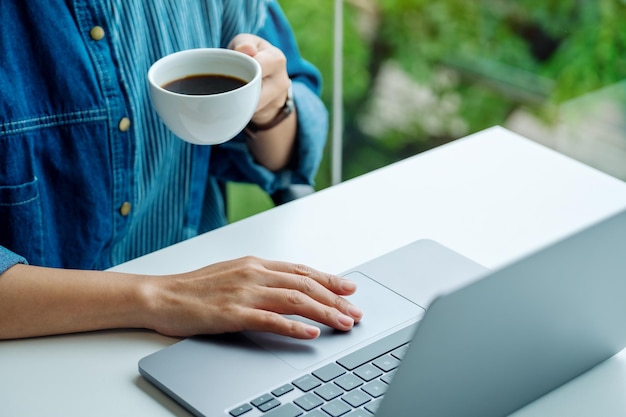Zbliżenie obrazu kobiety pracującej i dotykającej touchpada laptopa podczas picia kawy w biurze