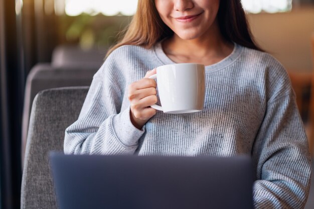 Zbliżenie obrazu kobiety pracującej na laptopie podczas picia kawy w kawiarni