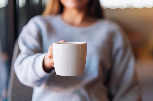 Zbliżenie obrazu kobiety trzymającej filiżankę kawy w kawiarni i pokazującej ją