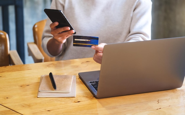 Zbliżenie obrazu kobiety trzymającej kartę kredytową podczas korzystania z inteligentnego telefonu i laptopa w biurze