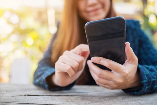 Zbliżenie obrazu kobiety trzymającej, używającej i patrzącej na telefon komórkowy w plenerze