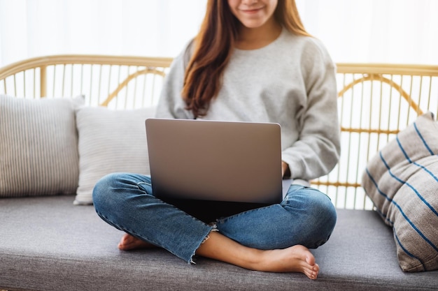 Zbliżenie obrazu młodej kobiety używającej i pracującej na laptopie, siedząc na kanapie w domu