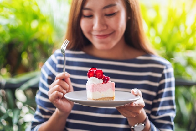 Zbliżenie obrazu pięknej młodej azjatyckiej kobiety trzymającej i jedzącej kawałek sernika truskawkowego