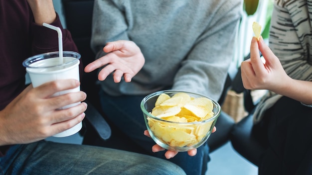 Zbliżenie obrazu przyjaciół pijących i jedzących chipsy ziemniaczane razem