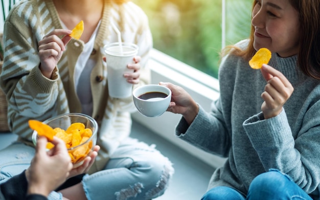 Zbliżenie obrazu przyjaciół pijących i jedzących chipsy ziemniaczane razem