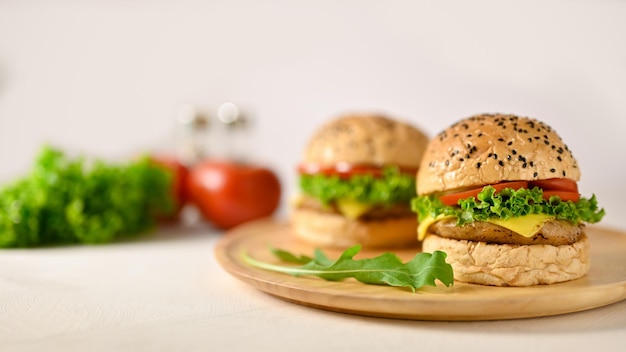 Zbliżenie obrazu pyszne hamburgery wołowe na drewnianym talerzu na biały stół ze świeżymi warzywami