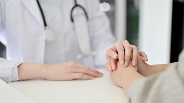 Zbliżenie obrazu troskliwej lekarki trzymającej ręce pacjenta, aby ją pocieszyć podczas spotkania