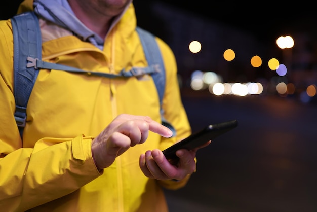 Zbliżenie obrazu turysty z plecakiem za pomocą smartfona na czeku na taksówkę na ulicy