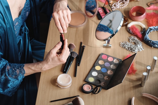 Zbliżenie: osoba transpłciowa siedząca przy stole za pomocą kosmetyków do makijażu