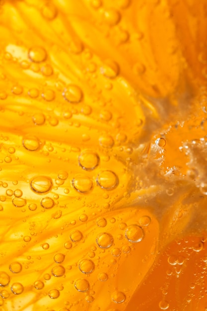 Zbliżenie pełnej klatki tła świeżego plasterka pomarańczy z miąższem w przezroczystym dżinie alkoholowym i napoju tonikowym z małymi bąbelkami