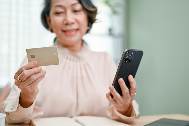 Zbliżenie piękna starsza kobieta Azji, trzymając smartfon i kartę kredytową