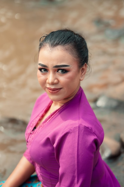 Zbliżenie pięknej azjatyckiej kobiety z makijażem, ubranej w tradycyjną fioletową sukienkę o nazwie kebaya