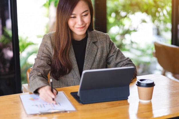 Zbliżenie piękny azjatykci bizneswoman pracuje cyfrową pastylkę i używa jako komputerowy komputer osobisty z pieniężnym dokumentem na stole