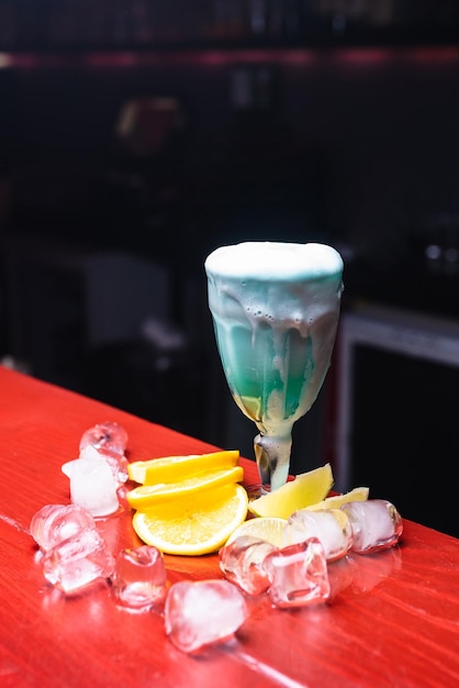 Zbliżenie piękny niebieski koktajl ozdobiony lodem i pomarańczą Szklanka z długą nóżką Barman przygotowuje drinki dla gości Nocne życie klubowe Świetna porcja koktajli